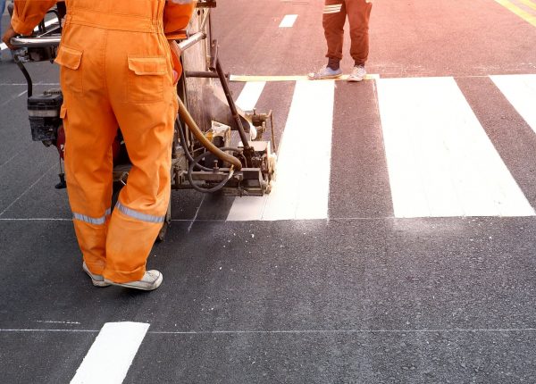 Low section of road workers using thermoplastic spray road marking machine to painting pedestrian crosswalk on asphalt road surface in the city